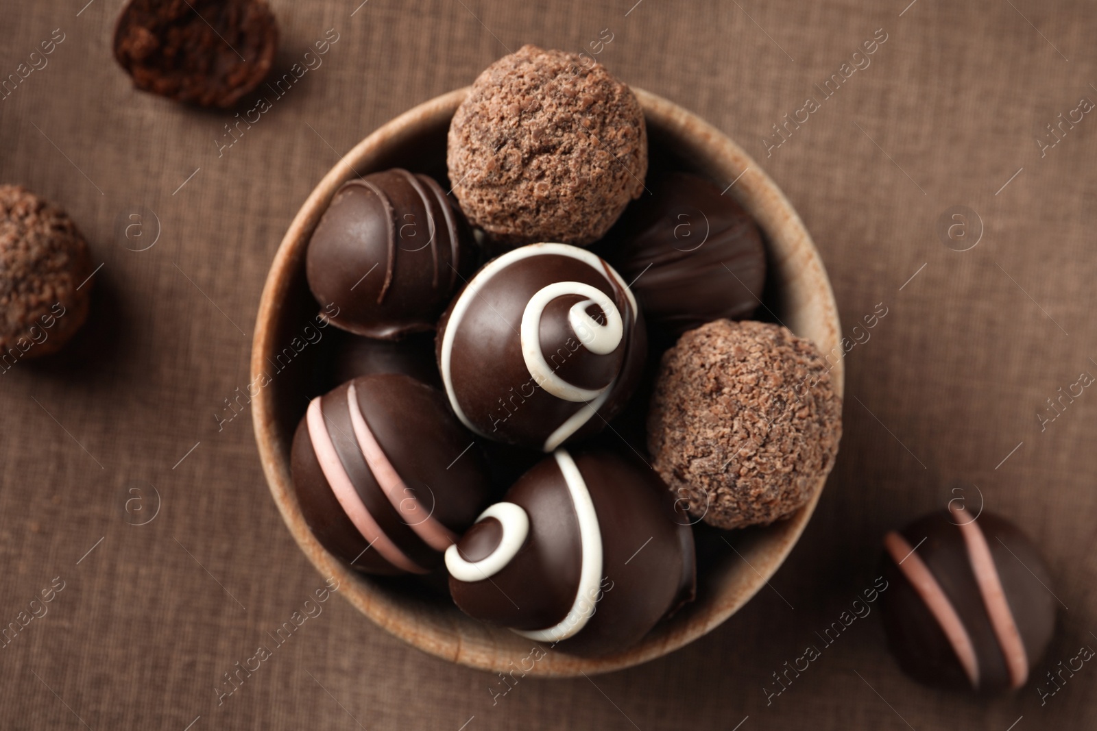 Photo of Many different delicious chocolate truffles on brown fabric, flat lay