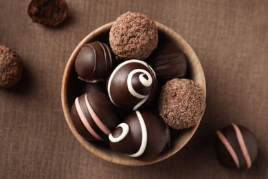 Many different delicious chocolate truffles on brown fabric, flat lay