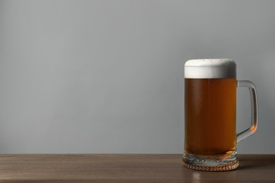 Glass mug of tasty dark beer on wooden table against grey background. Space for text