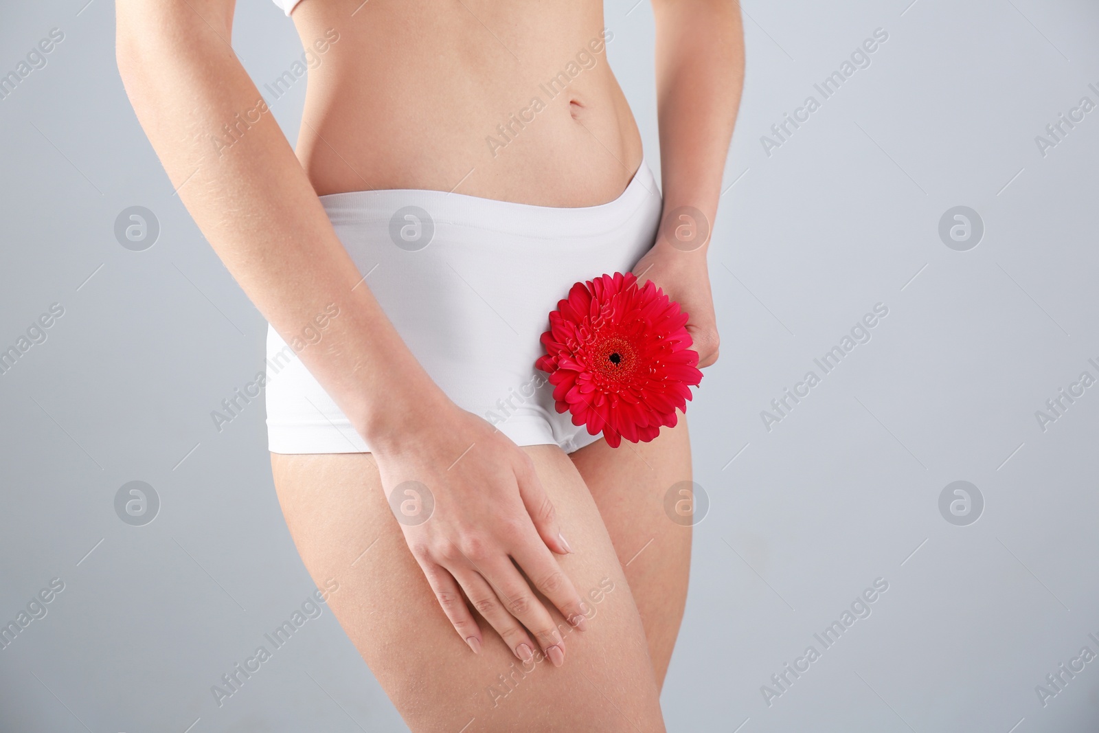 Photo of Young woman holding flower near underwear on grey background. Gynecology