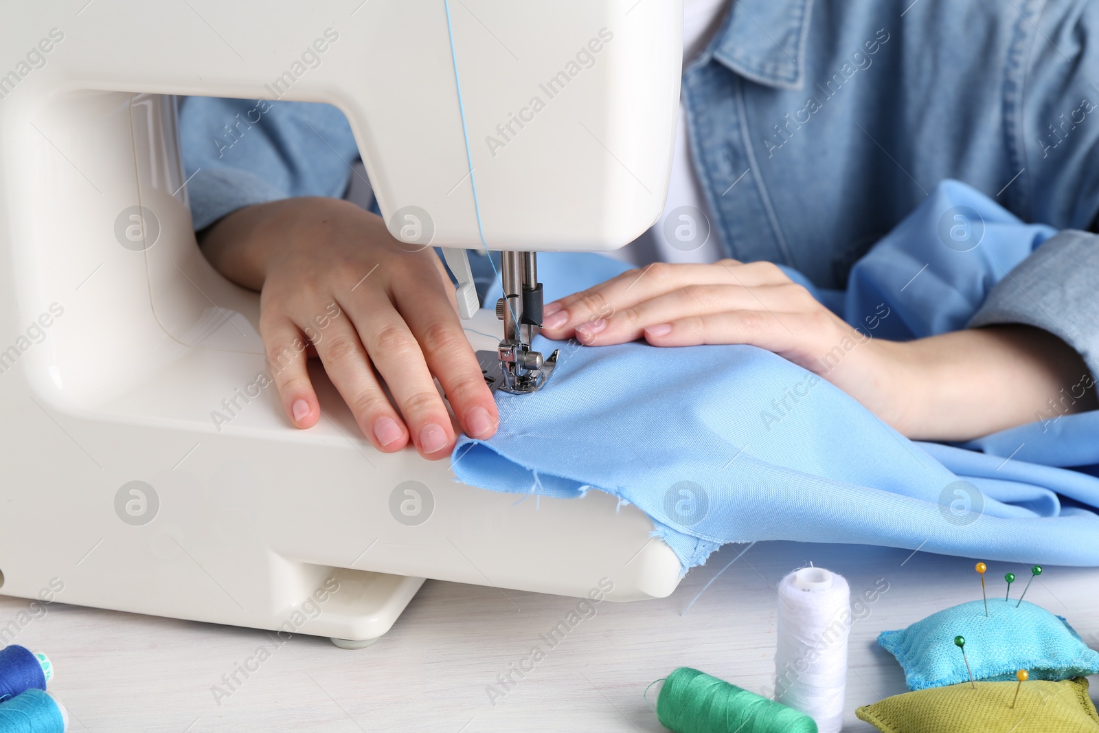 Photo of Seamstress working with sewing machine at white table indoors, closeup