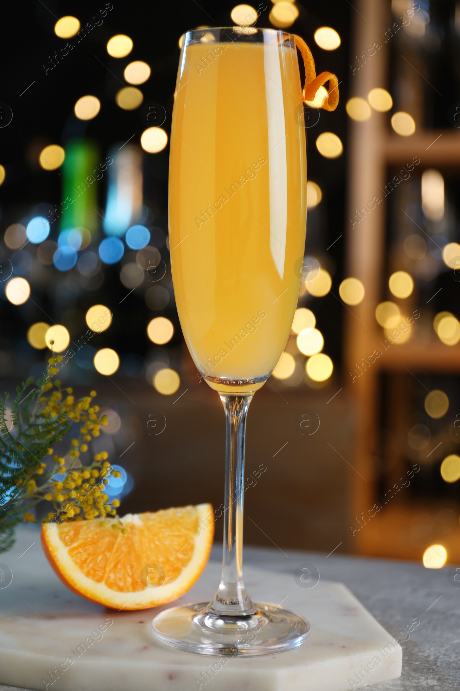 Photo of Mimosa cocktail with garnish and fresh fruit on bar counter against blurred lights