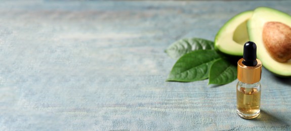 Photo of Bottle of essential oil and avocado on light blue wooden table. Space for text