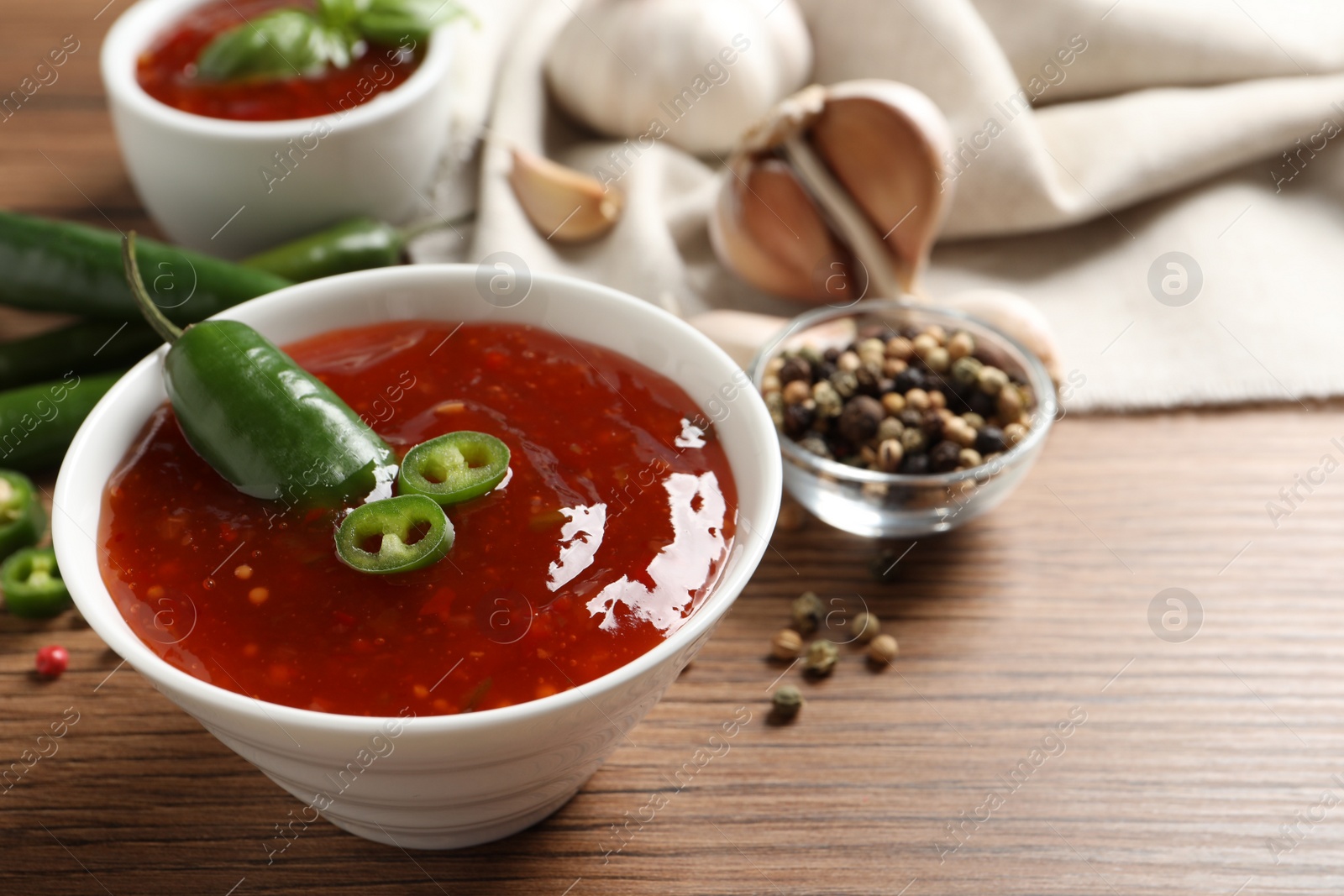 Photo of Spicy chili sauce in bowl on wooden table, space for text