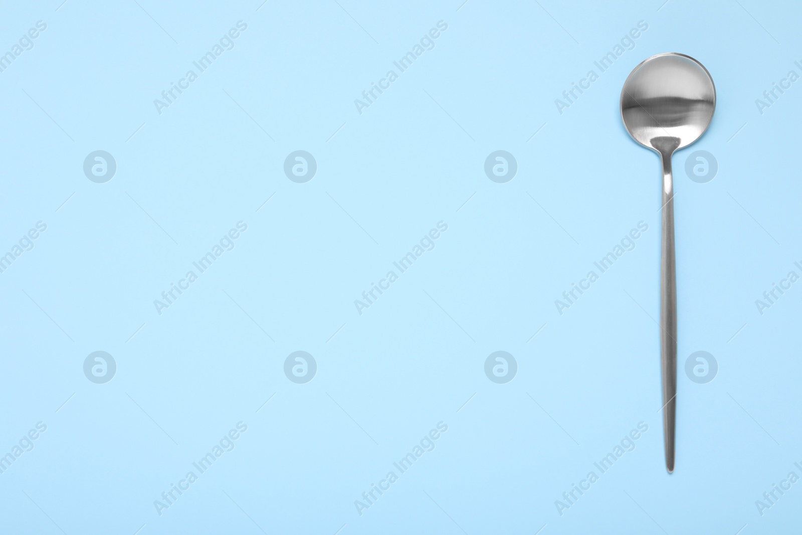 Photo of One shiny silver spoon on light blue background, top view. Space for text