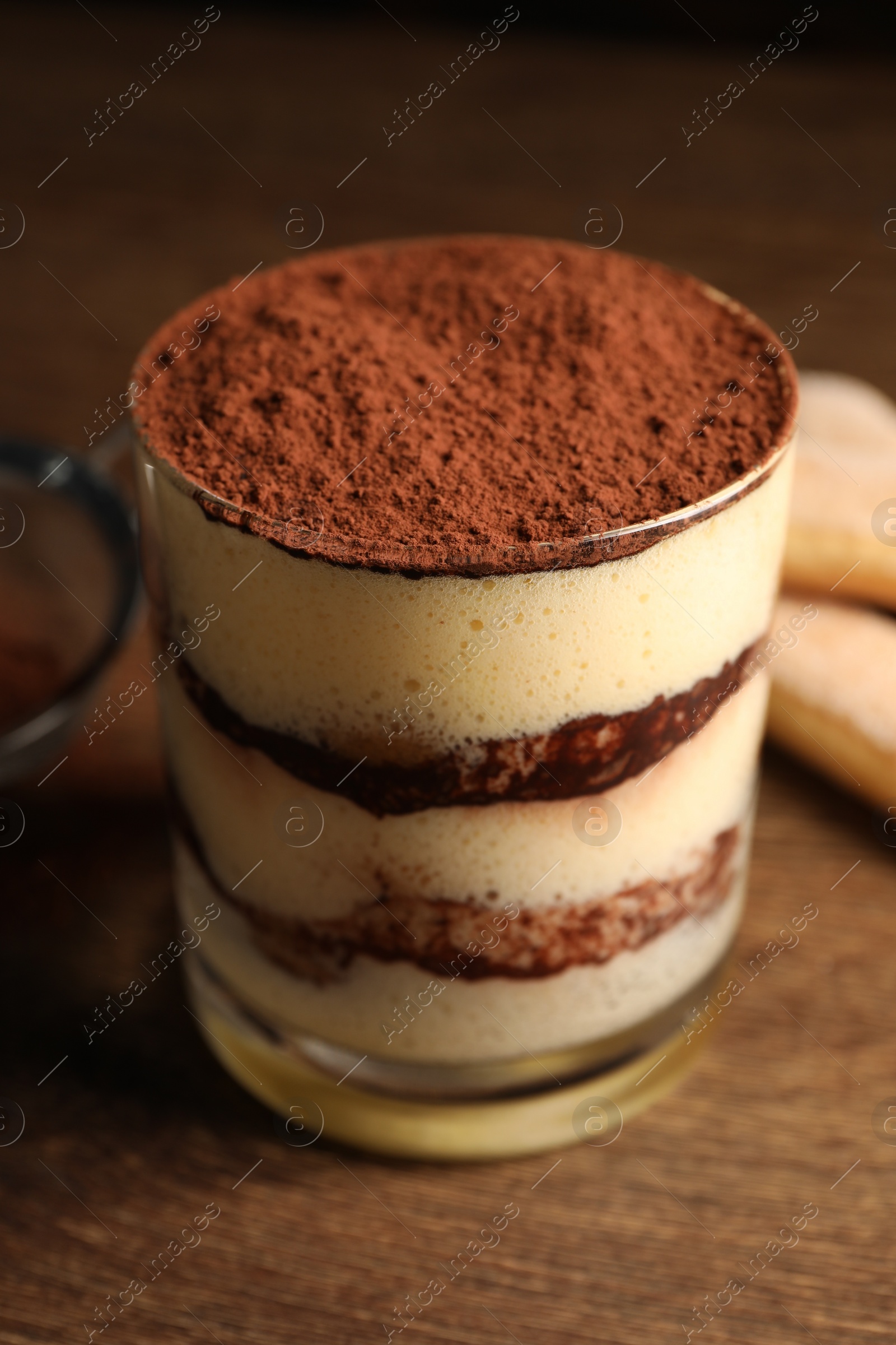 Photo of Delicious tiramisu in glass on wooden table, closeup