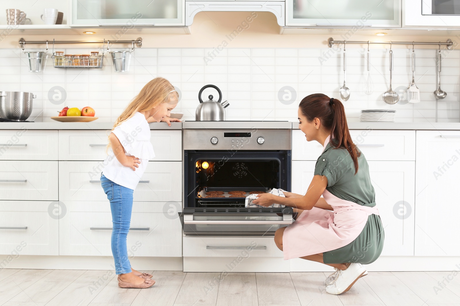 Photo of Young woman and her daughter baking cookies in oven at home