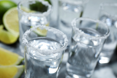 Mexican Tequila shots, lime slices and salt on grey table, closeup