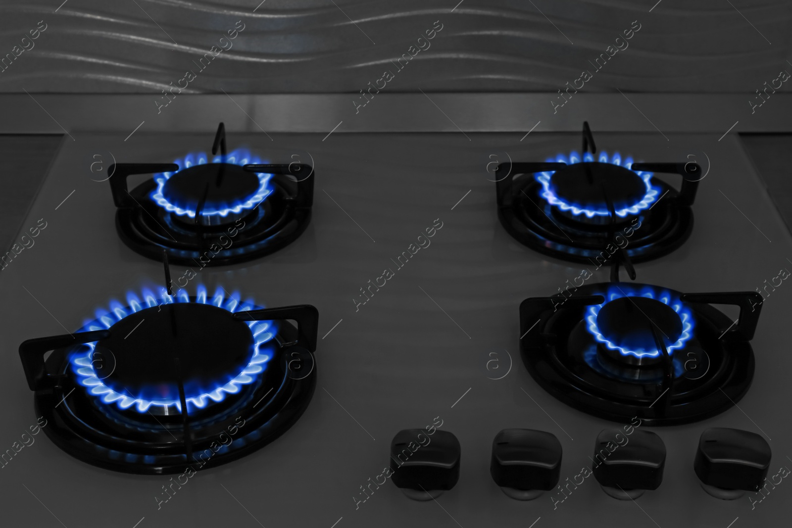 Photo of Modern gas cooktop with burning blue flames in kitchen at night