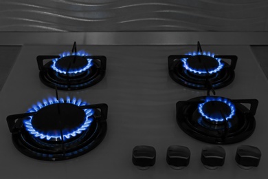 Modern gas cooktop with burning blue flames in kitchen at night