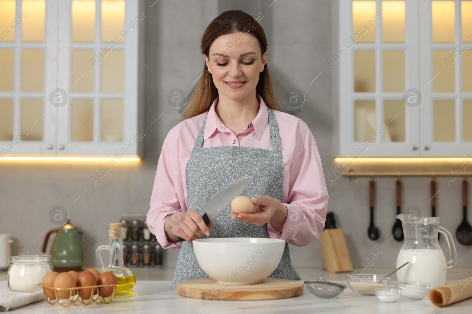 Photo of Making bread. Woman putting raw egg into bowl at white table in kitchen