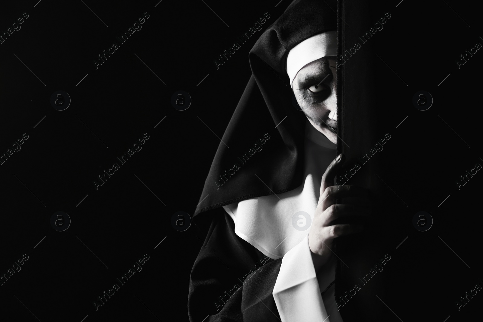 Photo of Scary devilish nun hiding on black background, space for text. Halloween party look