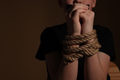 Photo of Little boy with tied arms taken hostage on dark background, closeup. Space for text