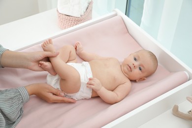 Mother changing her baby's diaper on table at home