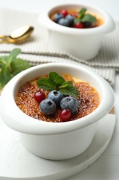 Photo of Delicious creme brulee with berries and mint in bowl on white table, closeup
