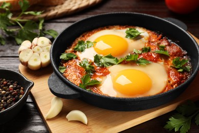 Photo of Delicious shakshuka in frying pan and spices on wooden table, closeup