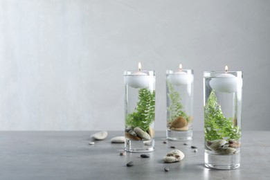 Photo of Candles, stones and fern leaves in glass holders with liquid on grey table. Space for text