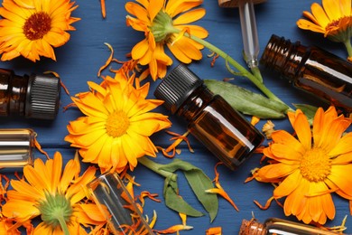 Photo of Bottles of essential oils and beautiful calendula flowers on blue wooden table, flat lay