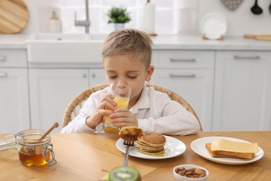 Photo of Breakfast time. Cute little boy drinking juice at table in kitchen