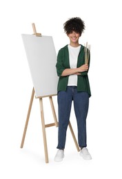 Photo of Young woman holding brush near easel with canvas against white background