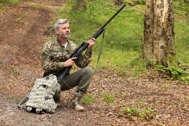 Photo of Man with hunting rifle and backpack wearing camouflage in forest. Space for text