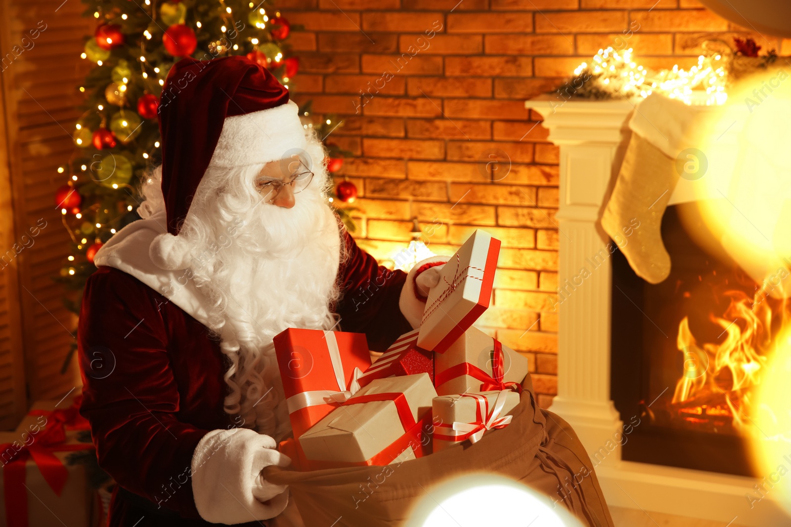 Photo of Santa Claus with sack of gifts in festively decorated room