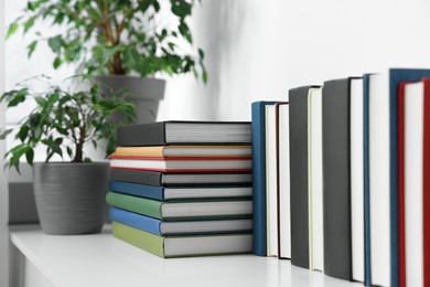 Many different books and potted plants on white shelf indoors