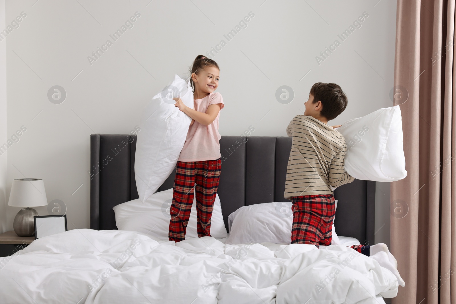 Photo of Brother and sister having pillow fight while changing bed linens in bedroom