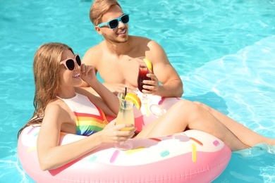 Young couple with cocktails in pool on sunny day