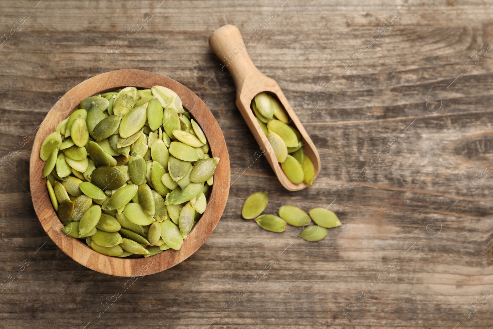 Photo of Bowl and scoop with peeled pumpkin seeds on wooden table, flat lay. Space for text