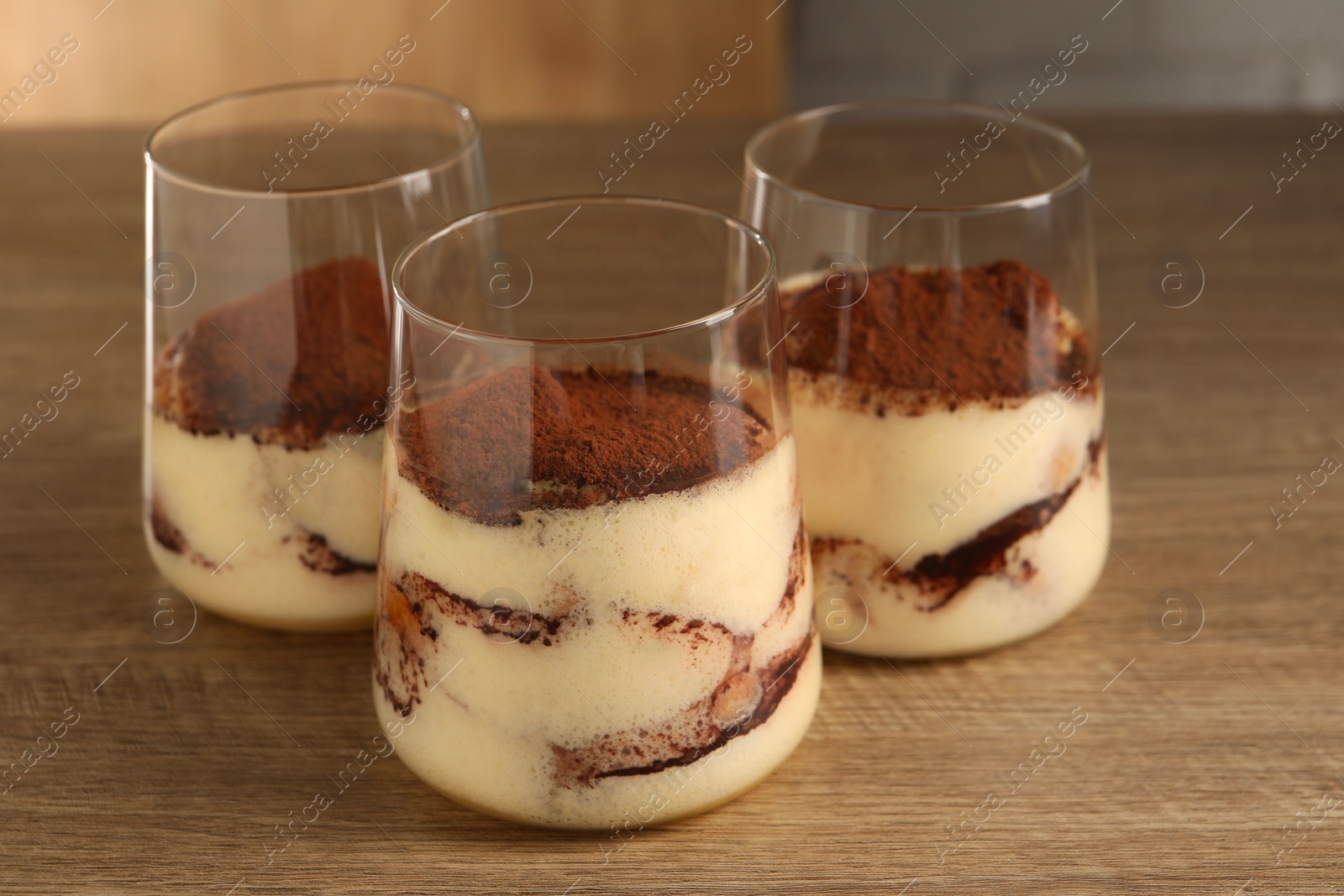 Photo of Delicious tiramisu in glasses on wooden table, closeup