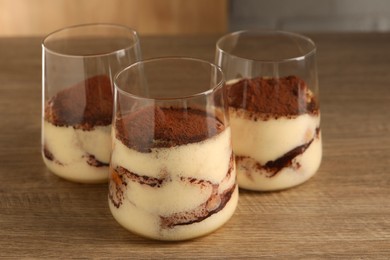 Photo of Delicious tiramisu in glasses on wooden table, closeup