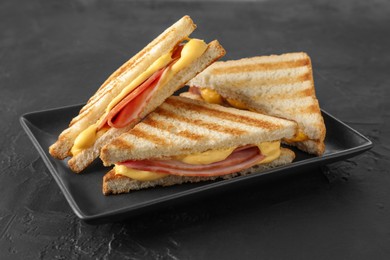 Photo of Tasty sandwiches with ham and melted cheese on black textured table, closeup