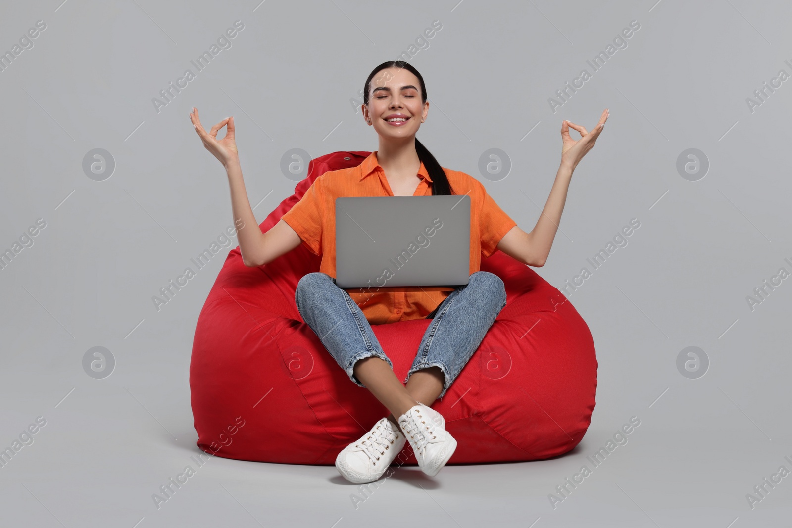 Photo of Happy woman with laptop sitting on beanbag chair and meditating against light gray background