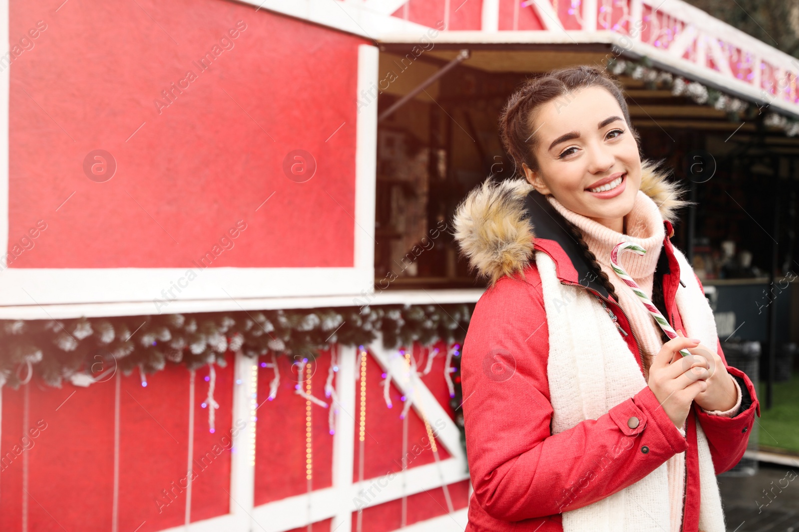 Photo of Young woman with candy cane spending time at Christmas fair