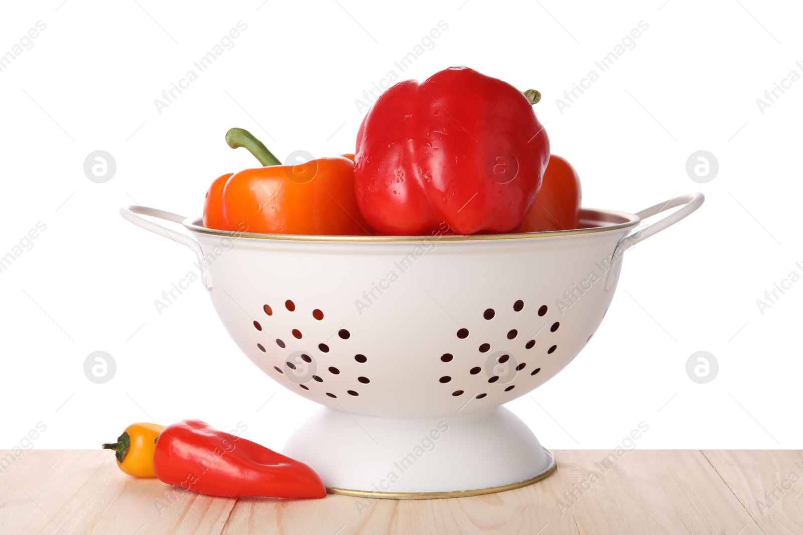 Photo of Fresh bell peppers in colander on wooden table against white background