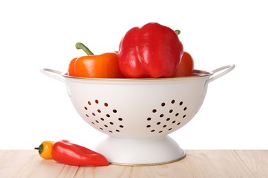 Photo of Fresh bell peppers in colander on wooden table against white background