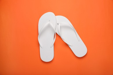 Stylish white flip flops on orange background, top view