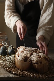 Photo of Woman cutting delicious Italian Easter dove cake (traditional Colomba di Pasqua) at wooden table, closeup