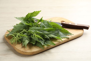 Photo of Board with fresh stinging nettle leaves on white wooden table
