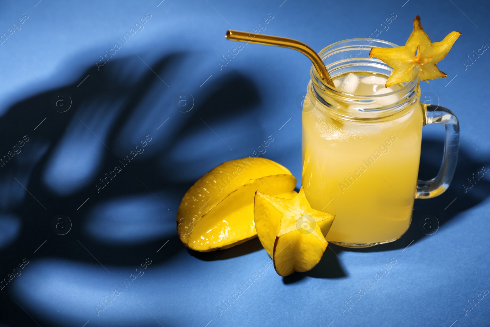 Photo of Delicious carambola juice and fresh fruits on blue background. Space for text