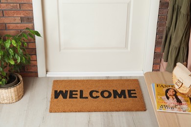 Door mat with word Welcome on wooden floor in hall