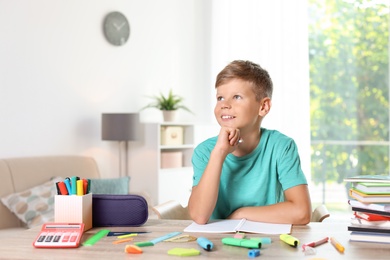 Photo of Little boy daydreaming while doing assignment at home. Stationery for school