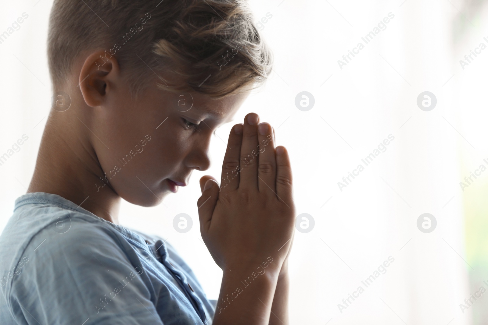 Photo of Little boy with hands clasped together for prayer on light background. Space for text