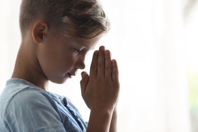 Little boy with hands clasped together for prayer on light background. Space for text