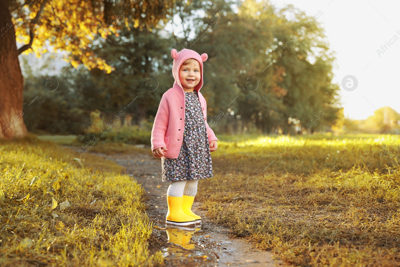 Photo of Little girl wearing rubber boots standing in puddle outdoors, space for text. Autumn walk