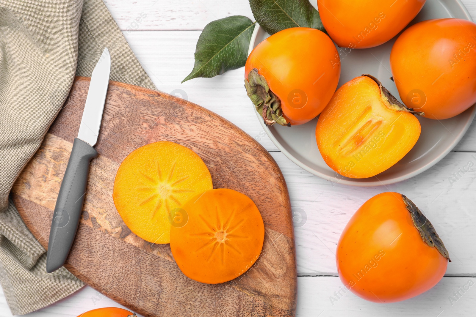 Photo of Delicious ripe juicy persimmons and knife on white wooden table, flat lay