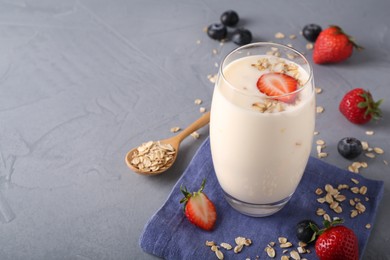 Tasty yogurt in glass, oats and berries on grey table, space for text