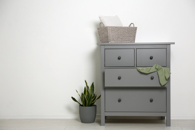 Grey chest of drawers near light wall. Space for text