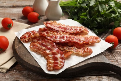 Photo of Fried bacon slices, tomato and parsley on wooden table, closeup